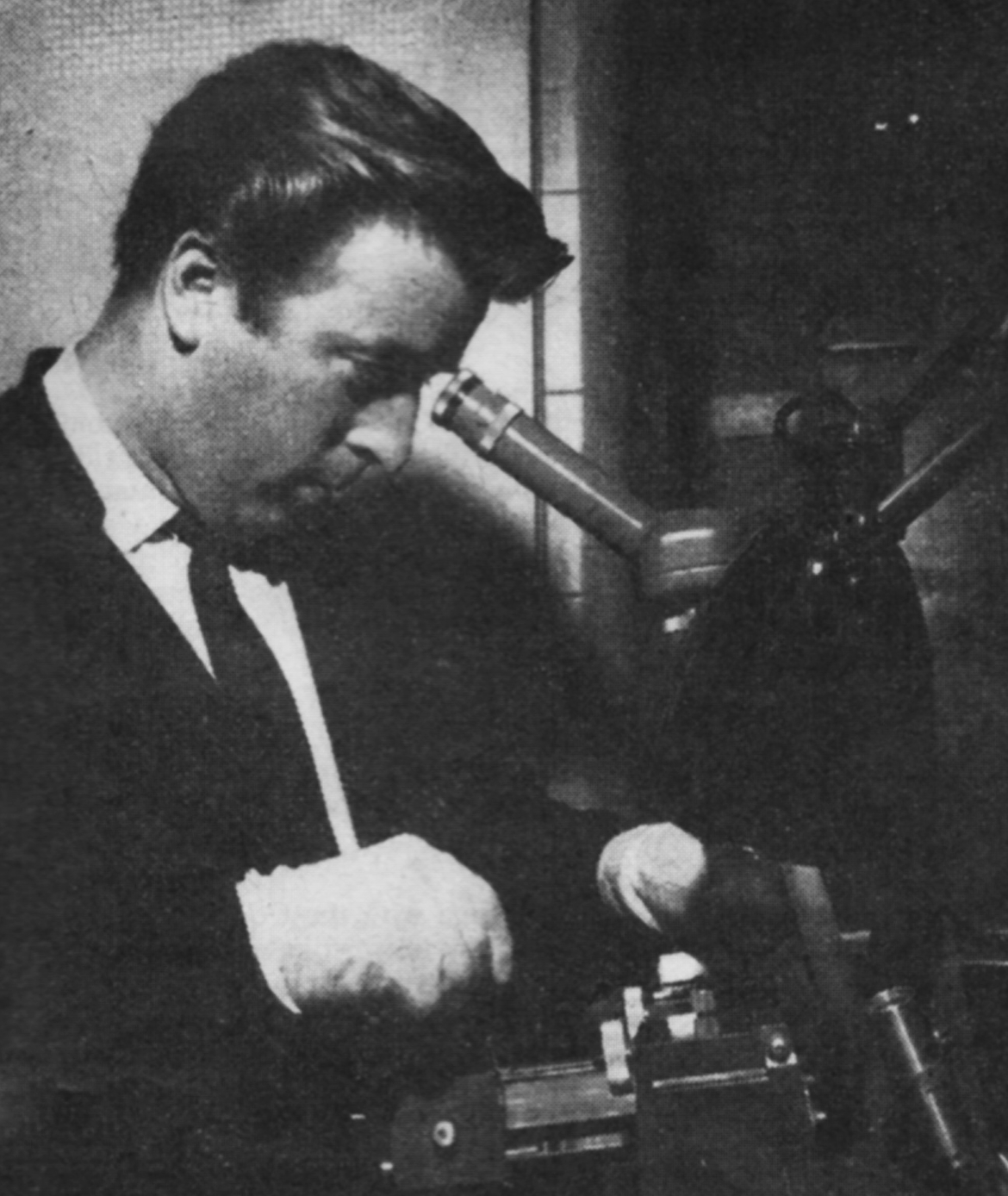 A man in gloves peers into a microscope-like viewer